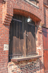 Detailed view of the brick facade of an old farmhouse with a clock and wooden gates used for loading and unloading the barn and storage.
