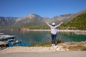 Fototapeta na wymiar Stylishly dressed girl in blue jeans, white hat, shirt and sneakers enjoys traveling during her spring vacation in the Kiparissi Lakonia village, Peloponnese, Zorakas Bay, Greece, May 2019.