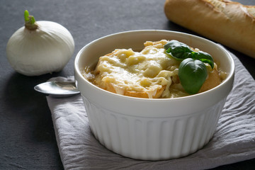 French onion soup in a white bowl on a dark gray background with baguette and parmesan cheese