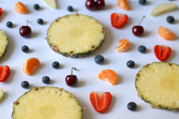 Various fruits and fruit slices on white background: pineapple, apple, strawberry, banana, blueberry, cherry and tangerine. Selective focus.