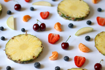 Various fruits and fruit slices on white background: pineapple, apple, strawberry, banana, blueberry, cherry and tangerine. Selective focus.