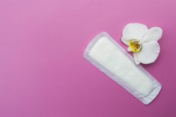 Sanitary napkin and white orchid flower on a pink background.