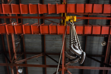 Metal hooks suspended on long chains of a monorail hoisting crane inside an industrial workshop, closeup.