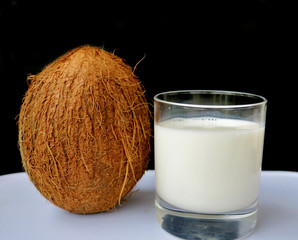 coconut milk with a big brown nut next to a black background