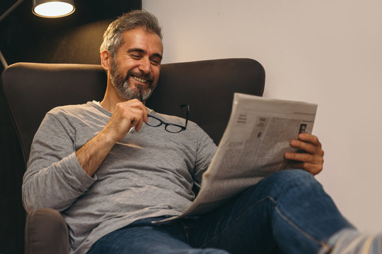 Middle Aged Happy Man Reading Newspaper Relaxed In His Sofa At Home