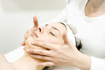 beautician worker gently massages face of  female costumer with special cream in beauty salon, close up