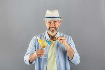 portrait of middle aged man summer dressed drinking cocktail on gray background