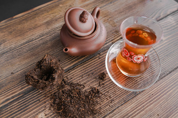 Black tea in traditional turkish tea cup with pattern on wooden table, traditional clay teapot with Puer tea near on wooden table. Black background. Horizontal image.