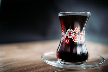 Black tea in traditional turkish tea cup with pattern on wooden table. Black background. Horizontal image.