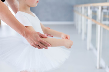Little ballerina is studying with ballet teacher in classical dance school. Female dance trainer is teaching kid girl to do choreographic position with hands. Practicing for children. Close up.