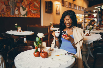 Elegant black woman sitting in a cafe. Businesswoman drinking a coffee. Woman use the phone