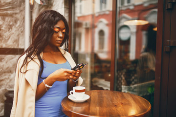 Elegant black woman standing in a cafe. Businesswoman  drainking a coffee. Woman use the phone