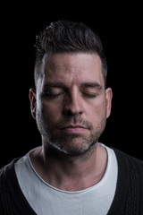 Obraz premium Studio portrait of a serious man with closed eyes. Isolated on black background. Vertical. Closeup.