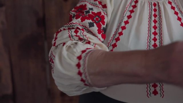 old woman in traditional Ukrainian clothes fixes sleeves on a shirt