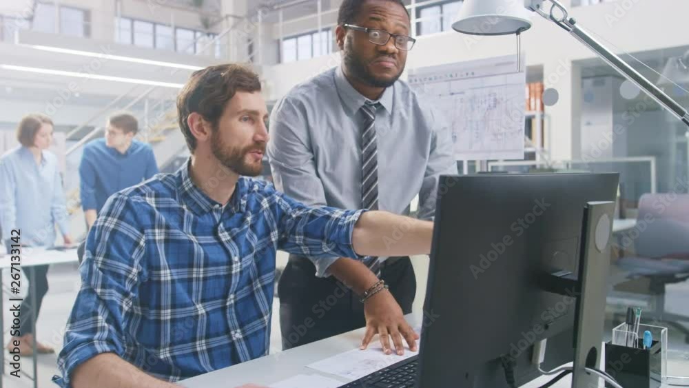 Poster In the Industrial Engineering Facility: Portrait of the Handsome Male Engineer Working on Desktop Computer, Chief Engineer Stands Beside and Explains Particularities of the Task and Project Details. 