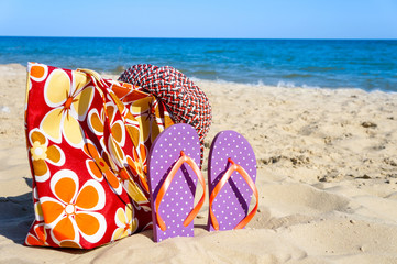 Summer beach hat, bag and flip flops on a sandy beach