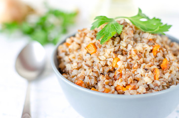 Buckwheat porridge with carrots and parsley in blue plate. On background of Golden onions and green parsley.