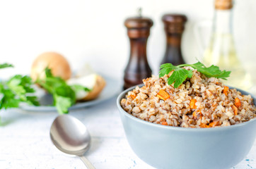Buckwheat porridge with carrots and parsley in blue plate. On background of Golden onions,green parsley and salt and pepper mills.