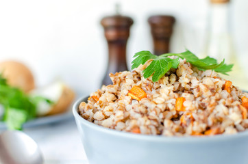 Buckwheat porridge with carrots and parsley in blue plate. On background of Golden onions,green parsley and salt and pepper mills.