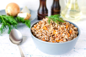 Buckwheat porridge with carrots and dill in a blue plate. On background of Golden onions, green dill and salt and pepper mills.
