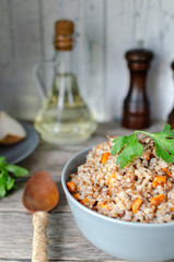 Buckwheat porridge with carrots and parsley in blue plate. On background of Golden onions,green parsley and salt and pepper mills.