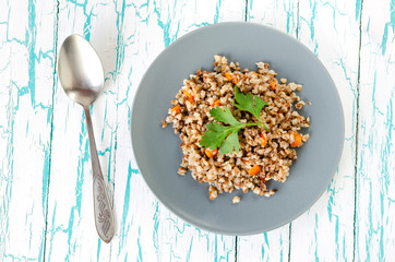 Buckwheat porridge with carrots and parsley on a light background in a gray plate.