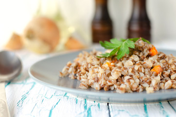 Buckwheat porridge with carrots and parsley in blue plate. On background of Golden onions,green...