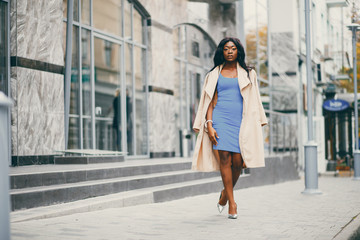 Fototapeta premium Elegant black woman standing in a autumn city. Businesswoman in a blue dress