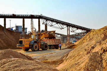 Fototapeta na wymiar Wheel front-end loader unloading sand into heavy dump truck. Crushing factory, machines and equipment for crushing, grinding stone, sorting sand and bulk materials - Image