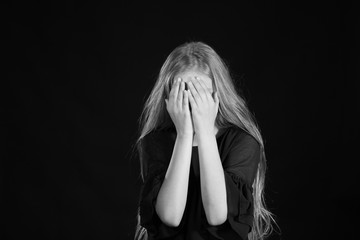 Portrait of a blonde girl with long hair on a black background. Emotional portrait.The girl shows different emotions on the face. Plays with long hair.