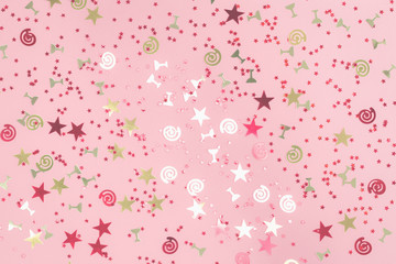 Golden stars flutes and swirls glitter and assorted sparkling confetti partially blurred on trendy pink background. Festive holiday pastel backdrop.