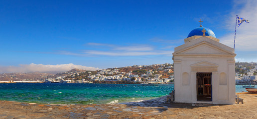 Whitewashed and blue domed Agios Nikolaos church in Mykonos, Greece, Europe. Panoramic view of old town and harbor: traditional greek village with white houses in Cyclades Islands.