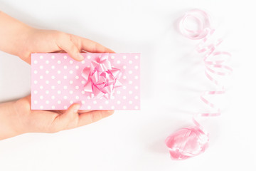 Hands holding a polka dot gift box or envelope with tender pink festive bow flower over wrapping ribbon roll isolated on white. Present and celebration or giveaway for feminine bloggers