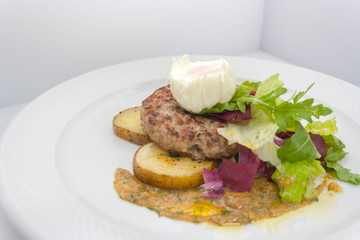 chopped beef cutlet on a pillow of potatoes with lettuce, poached egg and spicy gravy