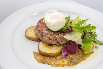 chopped beef cutlet on a pillow of potatoes with lettuce, poached egg and spicy gravy