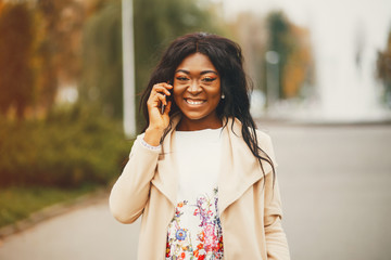 Elegant black woman standing in a autumn city. Businesswoman in a long coat. Lady use the phone