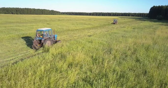 close motion above field haymakers drive towards each other cutting off grass for hay among immense farmland