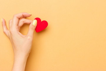 Female hand holding a red wooden heart on a warm yellow background