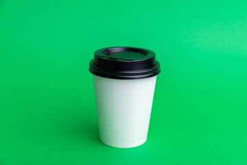 A white take away cup with black cap over green bakckground