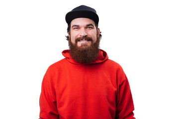 Portrait of  handsome  bearded guy in red hoody, black hat, looking at camera oer white background