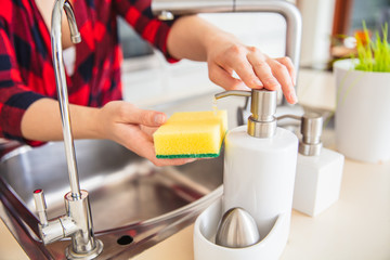 Woman is dosing the soap on the sponge in the kitchen.
