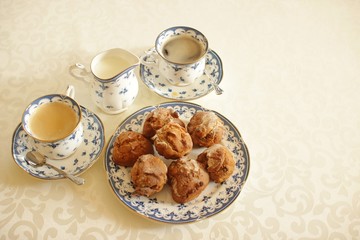 fresh cupcakes on a plate, milk jug and two cups of coffee from one set on a light tablecloth