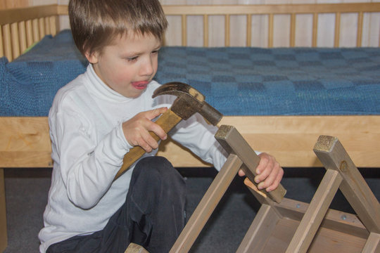 The boy is repairing a chair. Baby and hammer. The child makes himself.