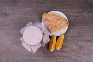 on a wooden background a plate with pancakes, a jar under a paper lid of a lemon wedge view from the top