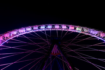 Part of ferris wheel in funfair at night.