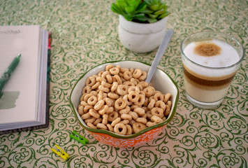 Cereal Cheerios Bowl with coffee, book, and flowers over green background 