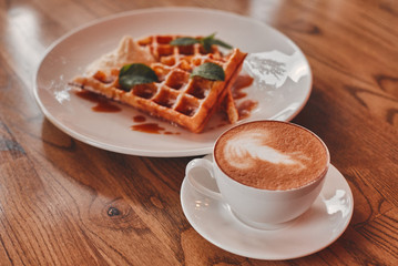 A cup of cappuccino with dessert on a wooden table