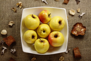 Yellow apples in a white plate on a burlap. 