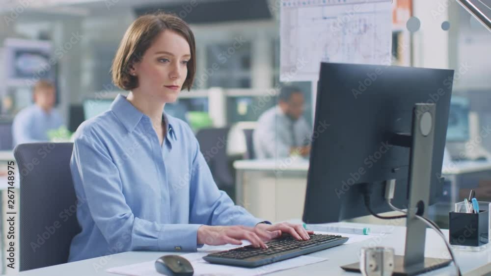 Poster In the Industrial Engineering Facility: Portrait of the Smart and Beautiful Female Engineer Working on Desktop Computer. In the Background Specialists and Technicians Working with Drafts and Drawings