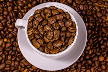 White cup filled with coffee beans on wooden table. Top view